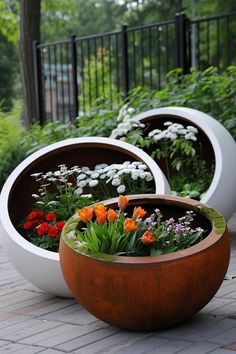 three planters with flowers in them sitting on the ground next to eachother