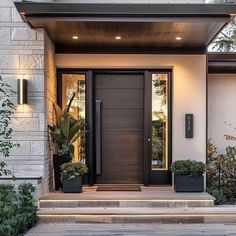 the front door of a modern home with potted plants on the steps and lights on