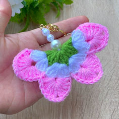 a hand holding a small crocheted butterfly brooch in pink, blue and green