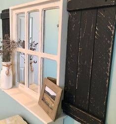 an old window is hung on the wall above a shelf with a vase and flowers