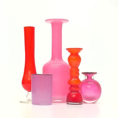 several different colored vases and glass containers on a white surface, including one pink