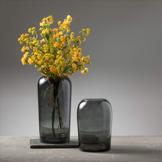 two vases with yellow flowers in them sitting on a table next to each other