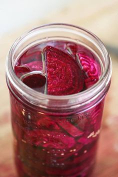 a jar filled with red liquid sitting on top of a wooden table next to a knife