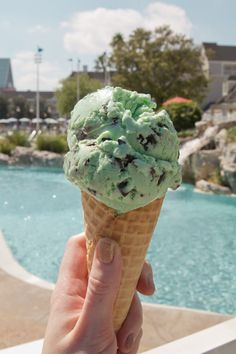 a hand holding an ice cream cone with chocolate chip cookies on it in front of a pool