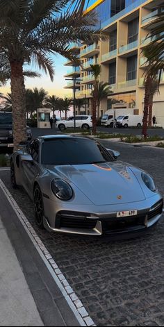 a silver sports car parked next to a palm tree in front of an apartment building