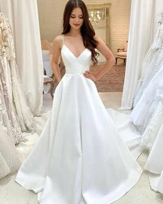 a woman in a white wedding dress standing next to dresses on mannequins