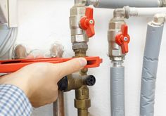 a person is fixing a water heater on the wall with red and gray pipes