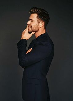 a man in a black suit is posing for the camera with his hand on his chin