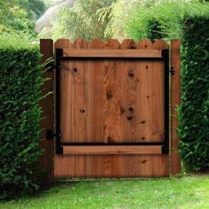 a wooden gate in the middle of a grassy area next to trees and shrubbery