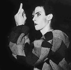 a black and white photo of a woman with her hand up to the side, pointing at something