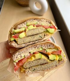 a person holding two sandwiches in their hands on a wooden table next to a donut