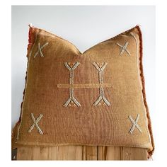 a brown pillow with cross stitching on the front and back, sitting on top of a wooden post