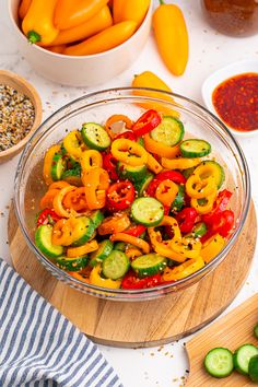 a bowl filled with peppers and cucumbers next to other ingredients on a cutting board