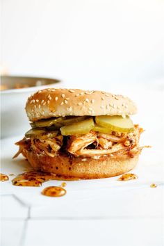 a pulled pork sandwich with pickles and cheese on a white tablecloth, ready to be eaten