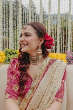 a woman in a pink and gold sari sitting on a couch with flowers around her neck