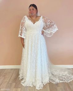 a woman in a white wedding dress standing next to a wall with her hands on her hips