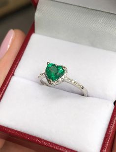 Featured is a dainty 1.0tcw natural emerald and diamond halo engagement, or right-hand ring. The center gemstone is a medium green, natural emerald handset in a 14K white gold prong setting. This natural gemstone has very good luster and eye clarity. Micro pave diamonds are placed delicately in the halo setting and mid-way down the shank. The diamonds are fully faceted and clean to the eye. Setting Style: Halo Setting Material: 14K White Gold Main Stone: Emerald Shape: Heart Measurements: 5.6 mm Emerald Heart-shaped Anniversary Rings, Emerald Heart Shaped Anniversary Rings, Green Diamond Heart Cut Ring, Heart-shaped Emerald Rings For Wedding, Emerald Wedding Jewelry For Valentine's Day, Formal Heart Cut Emerald Ring, Heart Cut Diamond Emerald Ring For Wedding, Green Fine Jewelry Heart Ring For Wedding, Green Heart Cut Jewelry With Center Stone