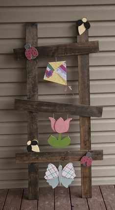 a wooden frame with paper flowers and birds on it, hanging from the side of a building