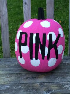 a pink polka dot pumpkin with the word pink painted on it sitting on a wooden bench