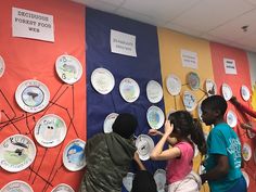 several children standing in front of a wall with plates on it and writing on the side