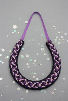 a purple and black braided necklace sitting on top of a silver table next to confetti