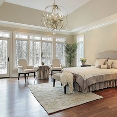 a large bed sitting in the middle of a bedroom next to two chairs and a chandelier