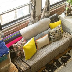 a couch with many pillows on it in front of a window and some windowsills