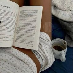 a person laying down reading a book and holding a cup of coffee