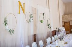 the table is set up with white linens and gold numbers on it, along with greenery