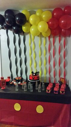 a mickey mouse themed birthday party with balloons and streamers on the wall, cake table