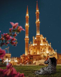 a woman sitting on the ground in front of a large building with two towers at night