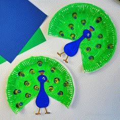 two paper plates with peacocks on them sitting next to a blue piece of paper