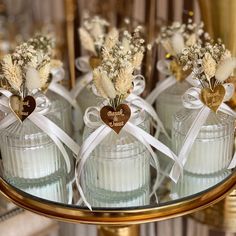 four glass jars with flowers in them sitting on a gold plated stand, decorated with white ribbon and heart shaped tags