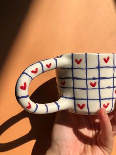 a hand holding a coffee mug with hearts painted on it's side and inside