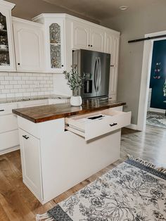 a kitchen with white cabinets and wood counter tops, an area rug on the floor