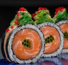 three sushi rolls are arranged on a blue plate with red and green toppings