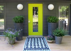 three potted plants on the front porch of a house with a yellow door and black and white checkered rug