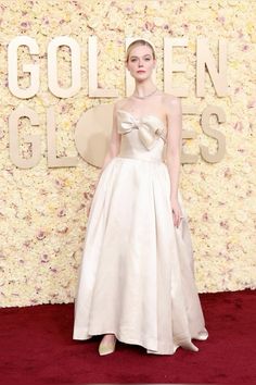 a woman in a white dress standing on a red carpet with flowers behind her and the words golden globes