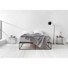 a bed sitting on top of a wooden floor next to a lamp and two tables