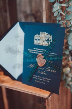 a blue and green wedding card with a gold button on it sitting on a wooden stand