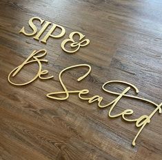 the words sips and be seated are made out of metal wire on a wood floor