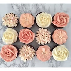 twelve cupcakes decorated with pink and white frosting flowers on a marble surface