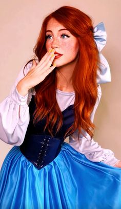 a woman with red hair wearing a blue dress and holding something in her mouth while posing for the camera