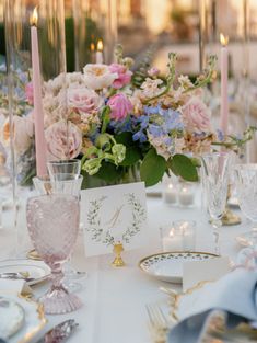 the table is set with pink and blue flowers, silverware, candles, and cards