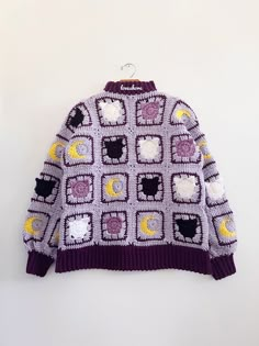 a purple sweater with sheep and moon patches on the front, sitting against a white wall