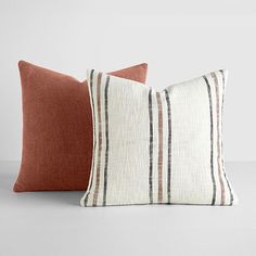 two orange and white striped pillows sitting on top of each other, one in the foreground