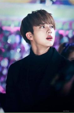 an image of a young man in black shirt looking up at something with blurry lights behind him