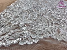 an image of a white lace fabric with flowers and leaves on the bottom, as seen from above