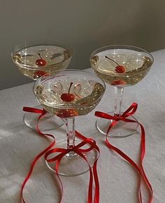 three wine glasses with cherries in them and red ribbons on the rims, sitting on a table