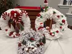 three christmas wreaths on a table with decorations in the shape of houses and snowmen